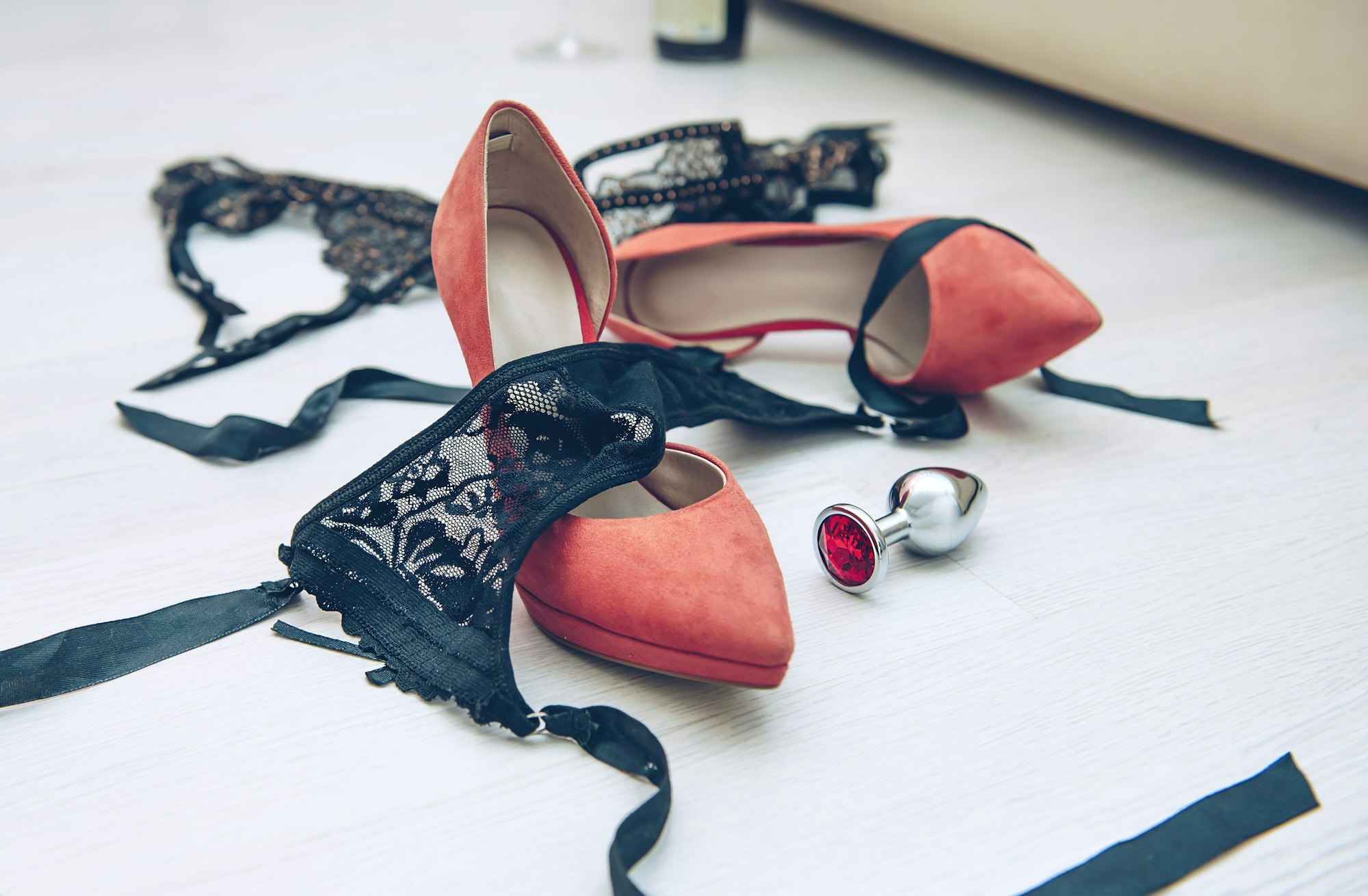 Beautiful black lingerie on the floor near the bed in the room with high-heeled shoes and anal plug.